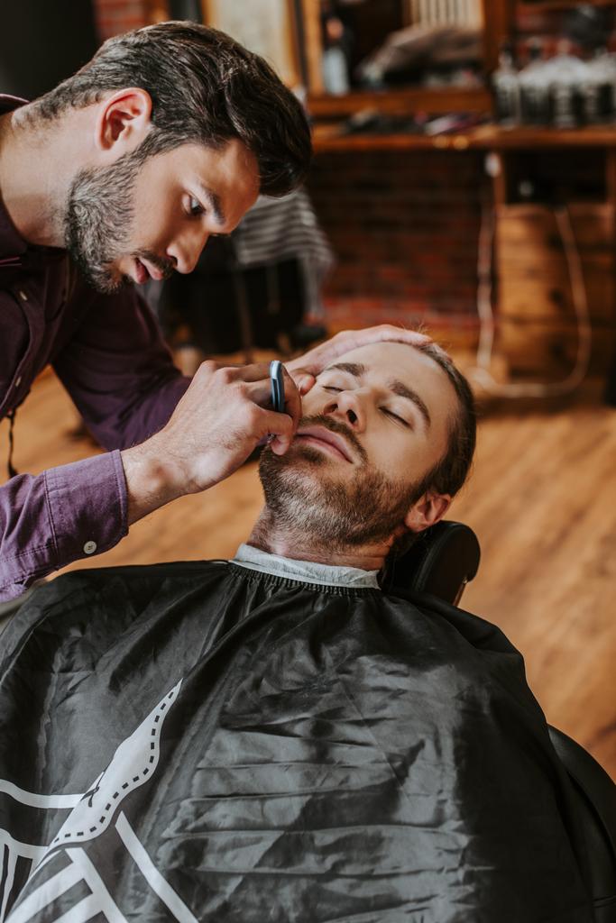 bonito barbeiro segurando navalha enquanto barbear homem
  - Foto, Imagem