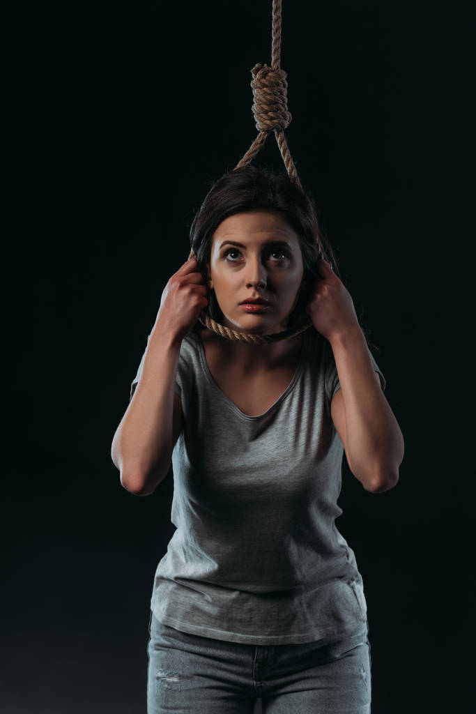 depressed young woman looking up while going to commit suicide by hanging herself isolated on black - Photo, Image