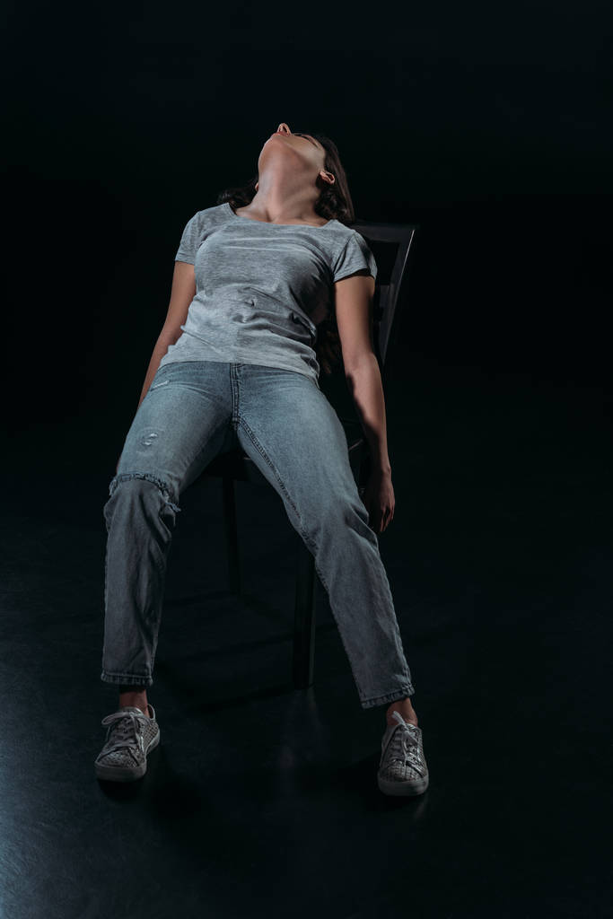 jonge, bewusteloze vrouw op stoel na het plegen van zelfmoord op zwarte achtergrond - Foto, afbeelding