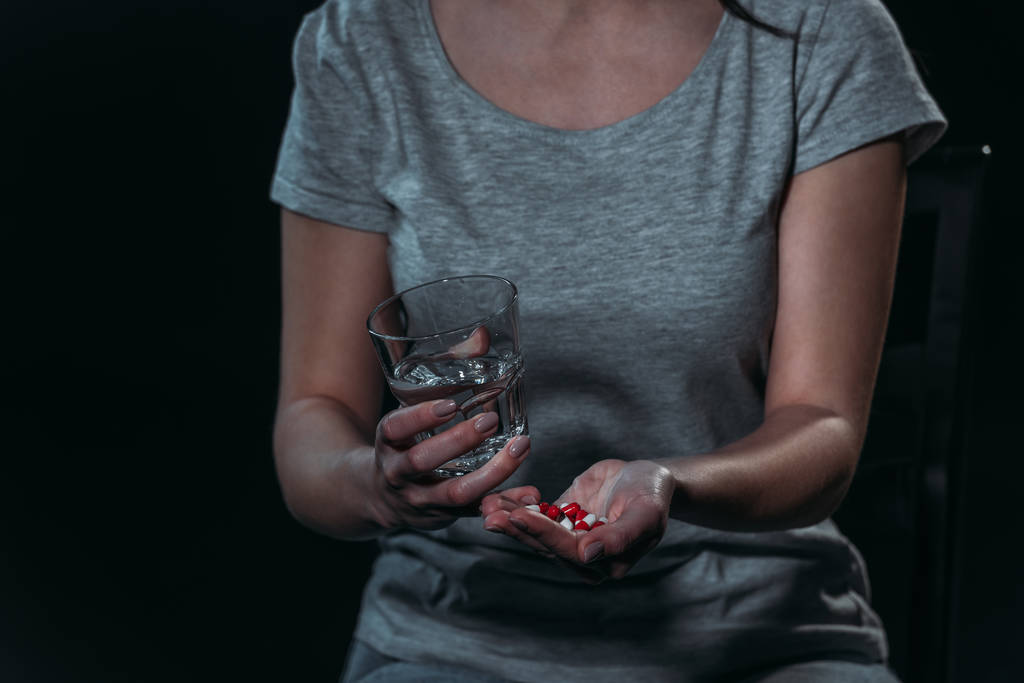 vista ritagliata di donna che va a suicidarsi e tenendo una manciata di pillole e bicchiere d'acqua isolato su nero isolato su nero
 - Foto, immagini