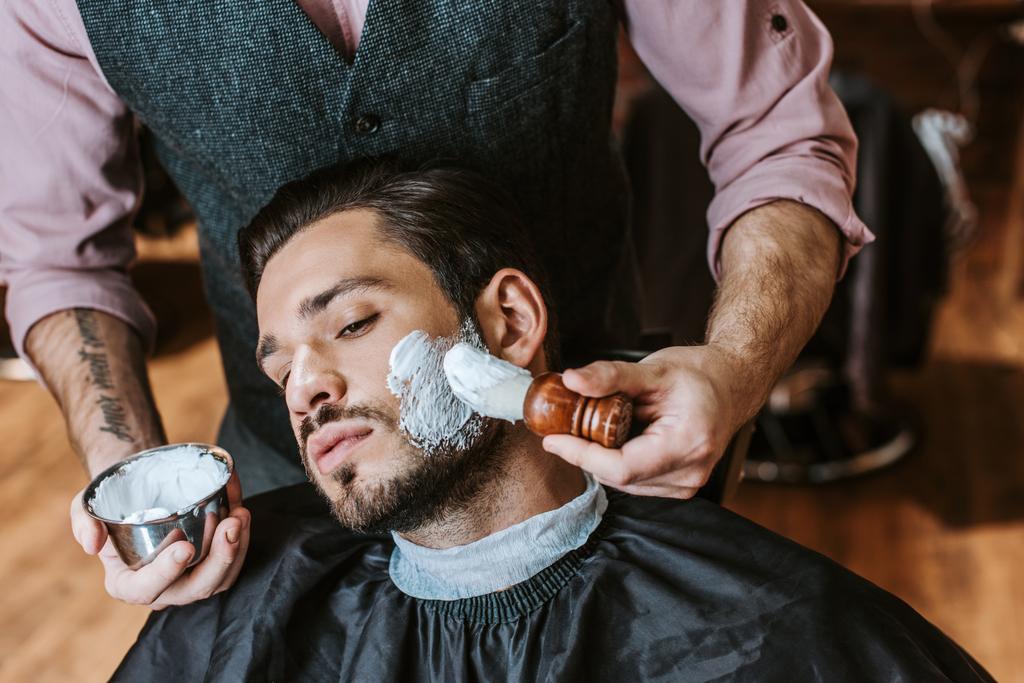 peluquero aplicación de crema de afeitar en la cara del hombre barbudo guapo
  - Foto, imagen