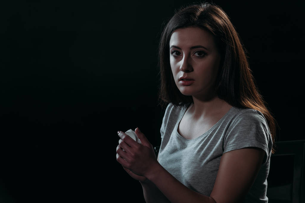 Frustrierte Frau blickt in die Kamera, während sie Selbstmord begeht, und hält Behälter mit Tabletten isoliert auf schwarz - Foto, Bild