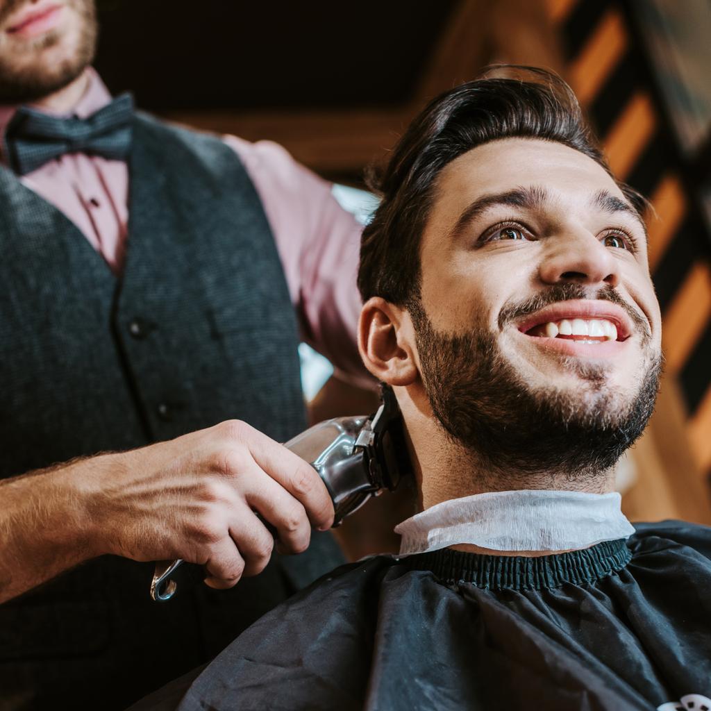vista angolo basso del trimmer tenuta barbiere mentre lo styling dei capelli di uomo felice in barbiere
  - Foto, immagini