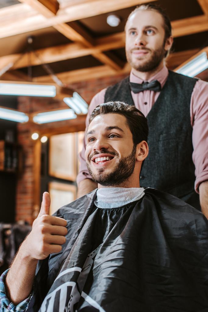 enfoque selectivo de hombre feliz mostrando el pulgar hacia arriba cerca de barbero
  - Foto, imagen