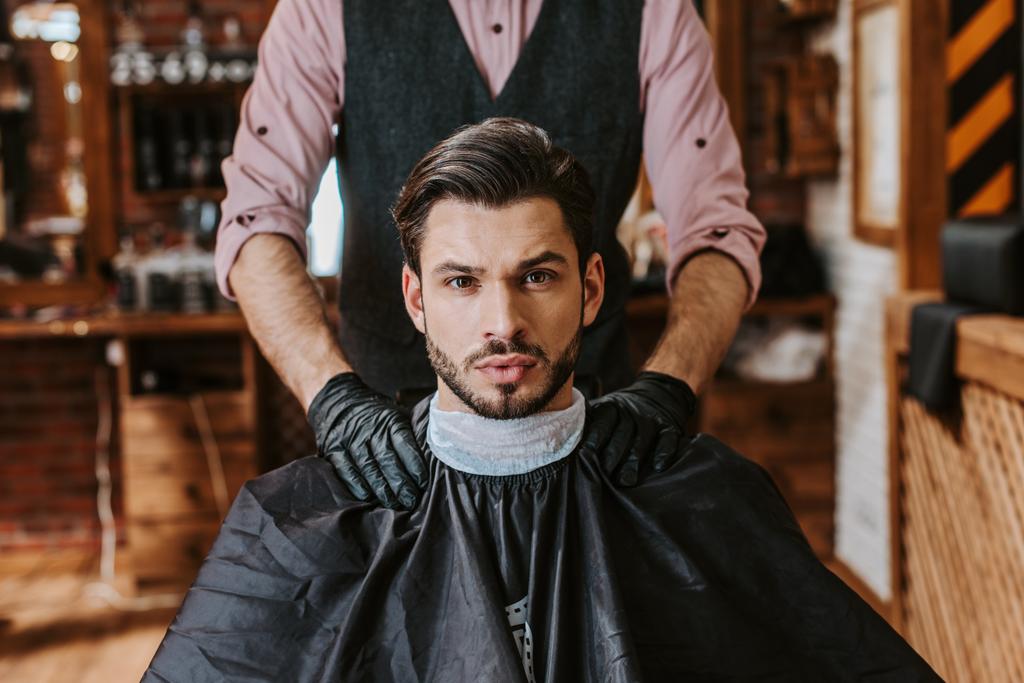 barbeiro em luvas de látex colocando as mãos sobre ombros de homem na barbearia
  - Foto, Imagem