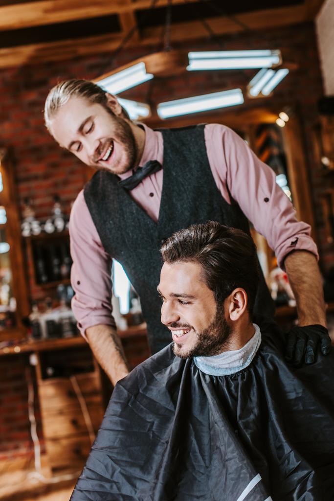 schöner Friseur in Latex-Handschuhen legt Hand auf Schulter eines glücklichen Mannes im Friseurladen  - Foto, Bild
