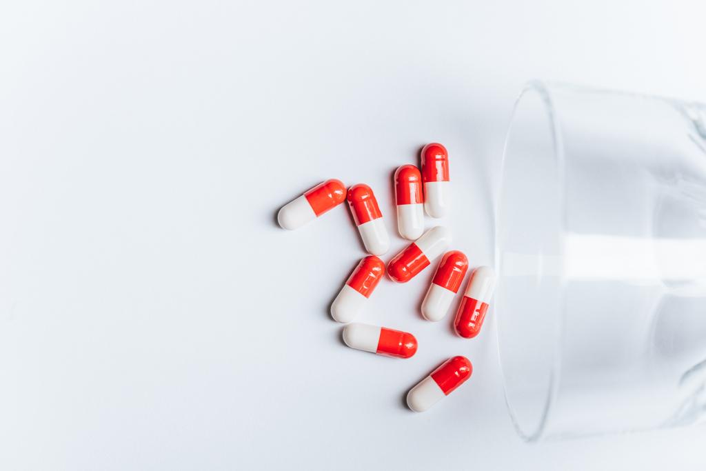 red and white capsules near overturned glass on white background, suicide prevention concept - Photo, Image