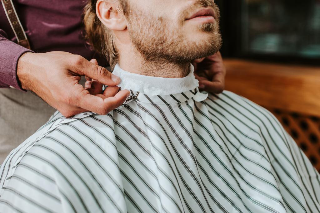 Ausgeschnittene Ansicht des Friseurs, der dem Mann einen Kragen um den Hals legt  - Foto, Bild