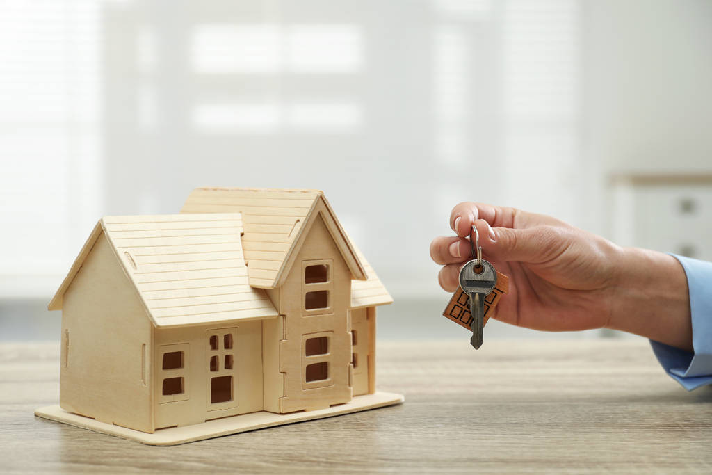 Immobilienmakler mit Hausmodell und Schlüssel am Holztisch, Nahaufnahme - Foto, Bild
