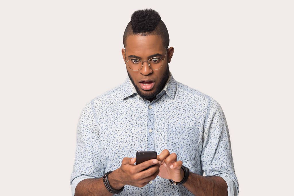 Verbazingwekkende Afro-Amerikaanse man op zoek naar telefoon met open mond - Foto, afbeelding