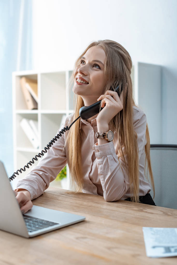 sorrindo agente de viagens falando ao telefone enquanto sentado no local de trabalho
 - Foto, Imagem