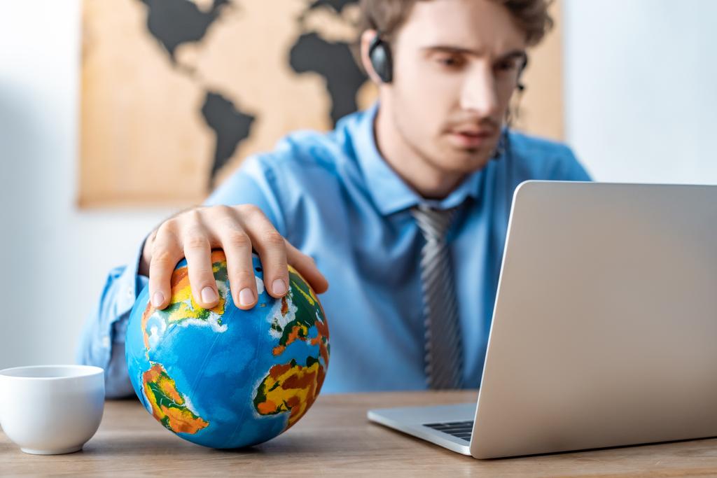 selective focus of travel agent touching globe while working near laptop - 写真・画像