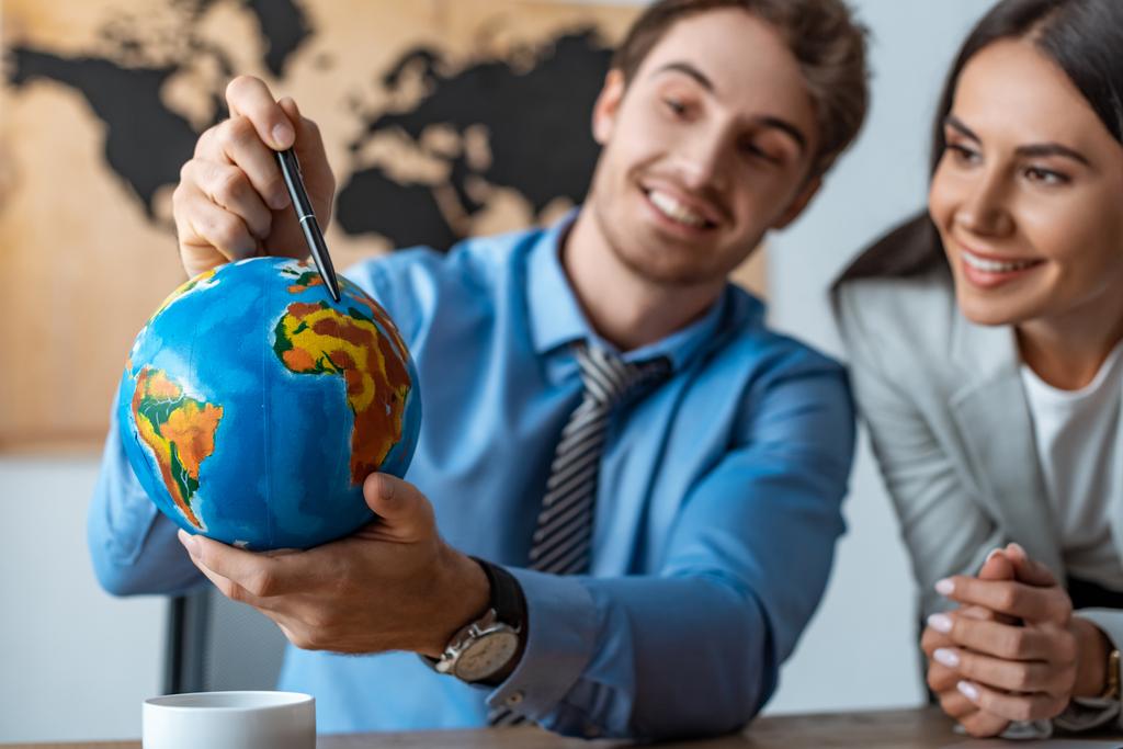 foyer sélectif de l'agent de voyage attrayant debout près d'un collègue souriant pointant avec stylo au globe
 - Photo, image