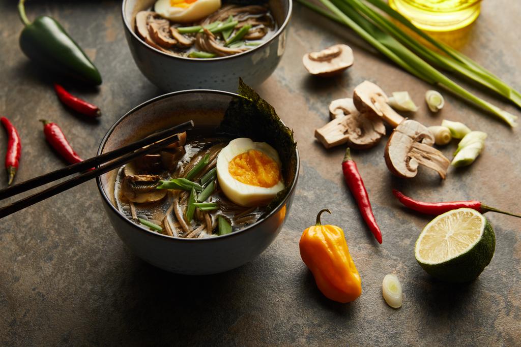 traditional spicy ramen in bowls with chopsticks and vegetables on stone surface - Photo, Image