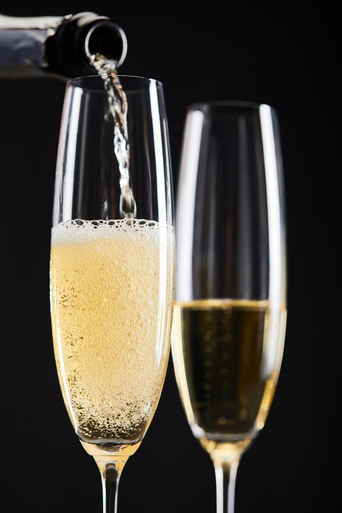 Nahaufnahme von Champagner, der zur Weihnachtsfeier in Gläser gegossen wird, isoliert auf schwarz  - Foto, Bild