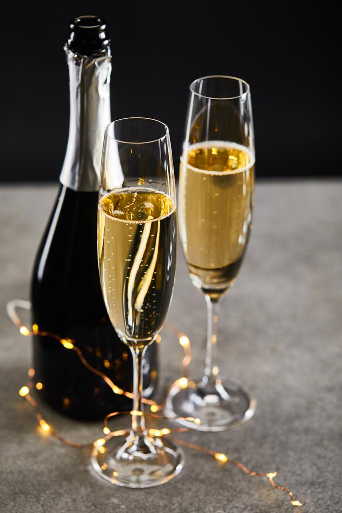 szemüveg és üveg pezsgővel és sárga karácsonyi fények, fekete - Fotó, kép