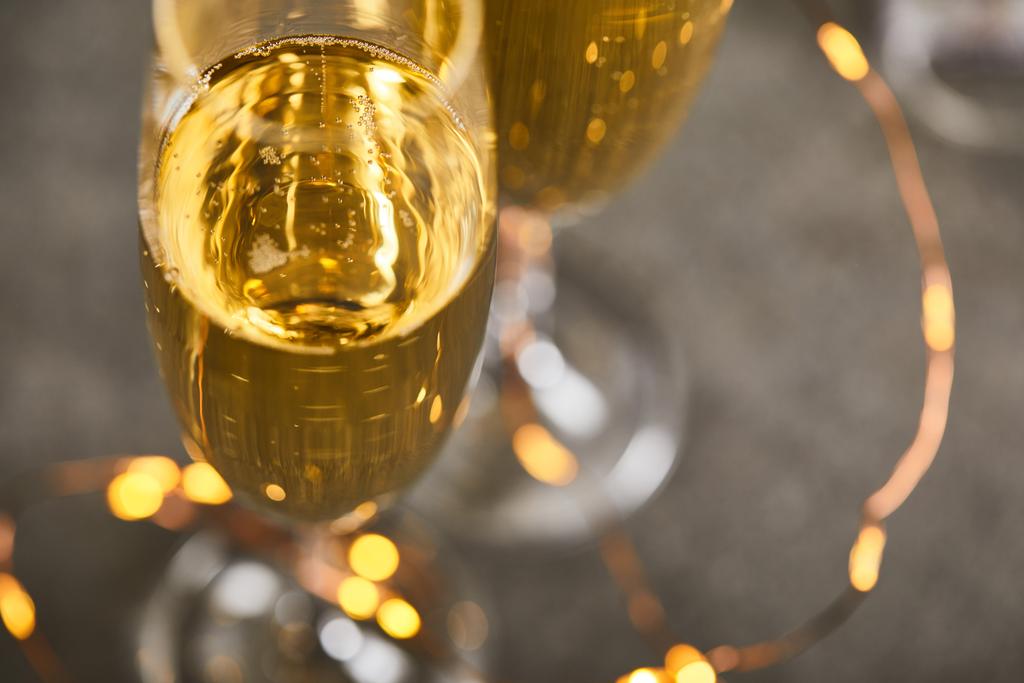 Bulanık sarı yılbaşı ışıklarıyla köpüklü şarap bardaklarını kapat. - Fotoğraf, Görsel