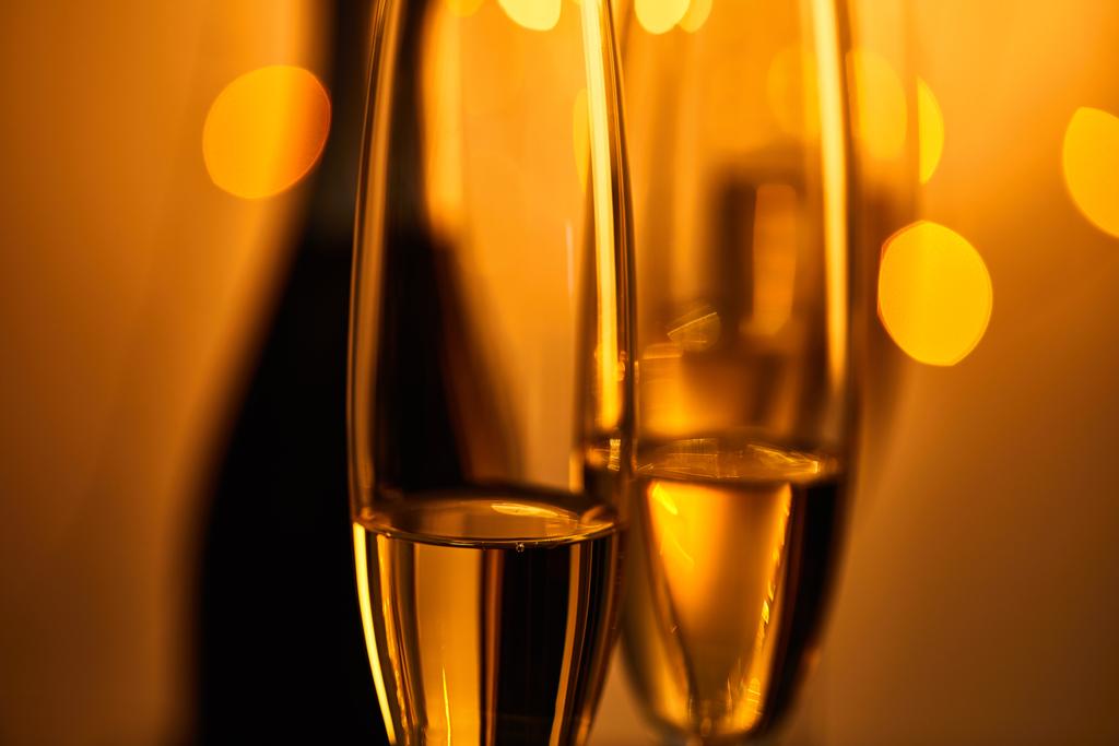 Бокалы игристого вина с размытой бутылкой и желтыми рождественскими огнями
 - Фото, изображение