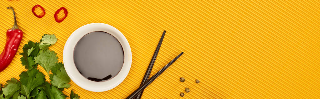 κορυφαία άποψη του τσίλι, σάλτσα σόγιας και κόλιανδρο κοντά chopsticks σε κίτρινο φόντο, πανοραμική λήψη - Φωτογραφία, εικόνα