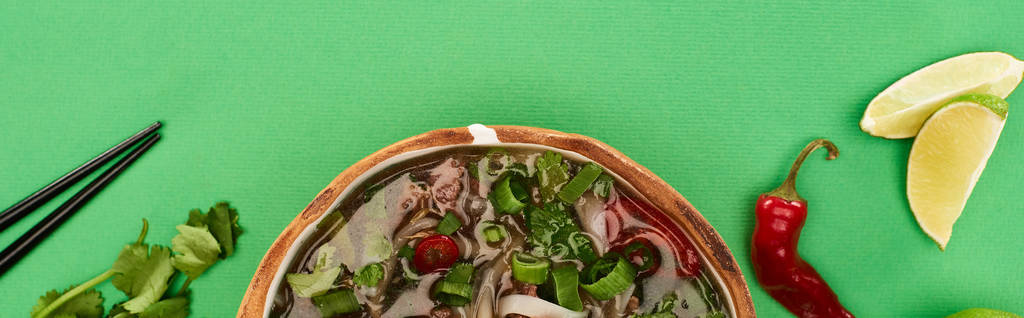 верхний вид фо в миске рядом палочки для еды, лайм, чили и кориандр на зеленом фоне, панорамный снимок
 - Фото, изображение