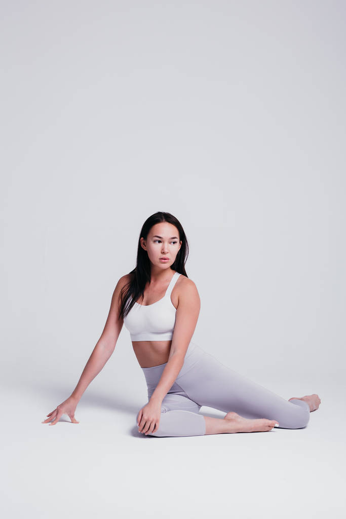 Giovane donna atletica che fa yoga su sfondo bianco il concetto di uno stile di vita sano e un equilibrio naturale tra il corpo e lo sviluppo mentale, in leggins grigi e t-shirt bianca
 - Foto, immagini
