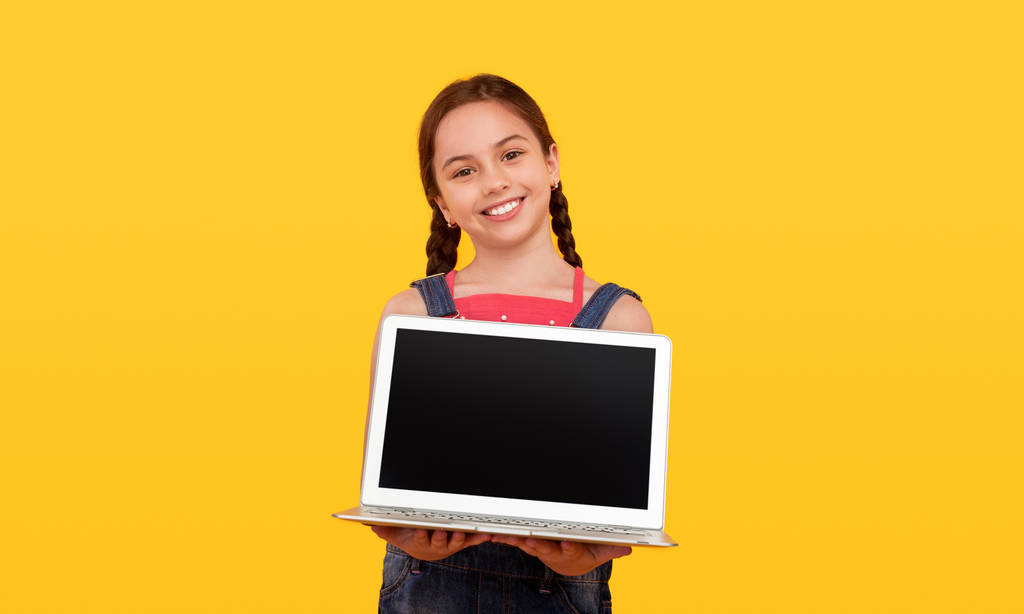 Vriendelijk schoolmeisje demonstreren laptop voor camera - Foto, afbeelding