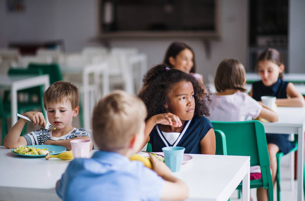 Група веселих маленьких школярів в їдальні, обідають
. - Фото, зображення