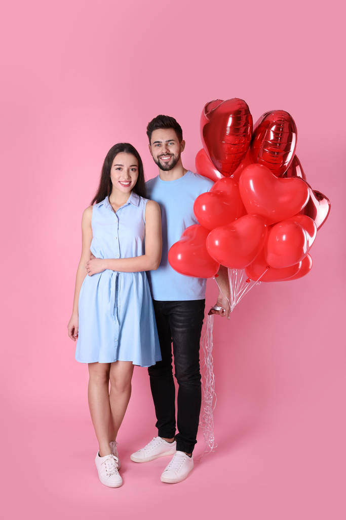 Preciosa pareja con globos en forma de corazón sobre fondo rosa. Celebración de San Valentín
 - Foto, imagen