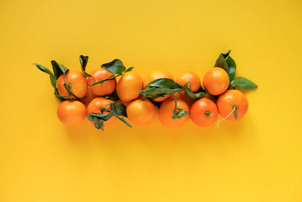 Mandarina naranja con hojas sobre fondo amarillo
 - Foto, Imagen