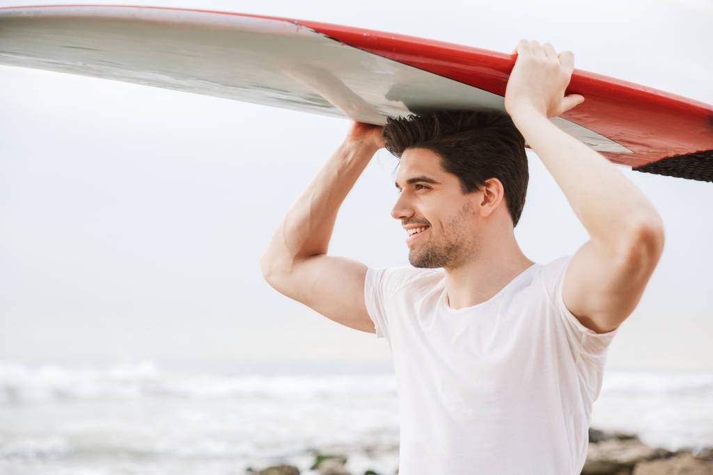 ハンサムな男サーファーでサーフィンでビーチの外. - 写真・画像