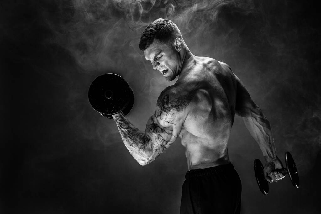 強力なスポーツマンは煙の中で重いダンベルを持ち上げる - 写真・画像
