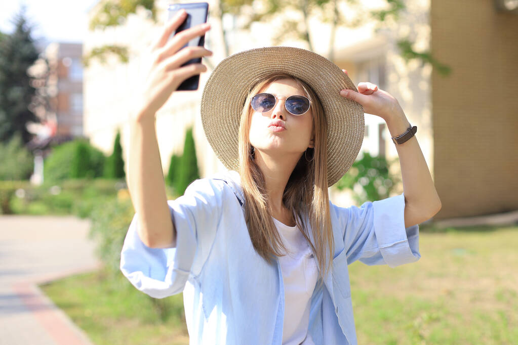 Hermosa chica rubia joven usando el teléfono móvil mientras está de pie al aire libre
. - Foto, imagen