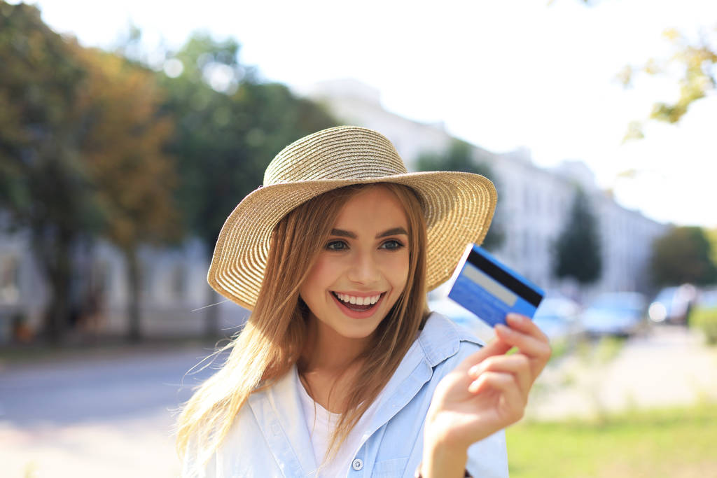 Веселая молодая оптимистичная девушка стоит на улице, держа кредитную карту в руке
. - Фото, изображение