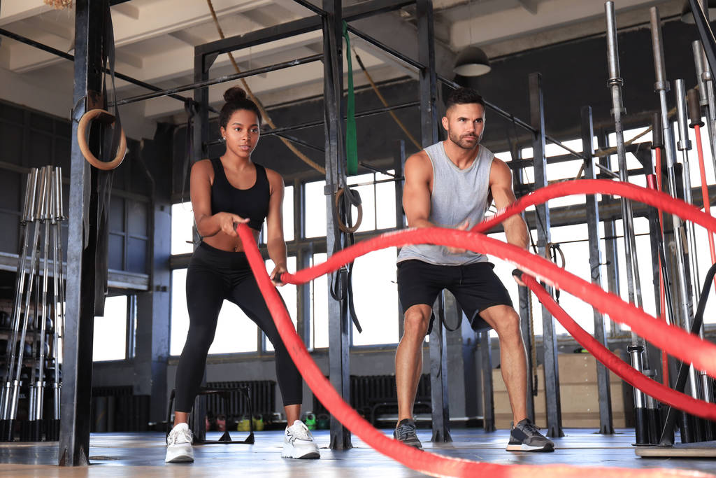 Atlétikai fiatal pár harci kötéllel gyakorolja a funkcionális edzés fitnesz terem. - Fotó, kép