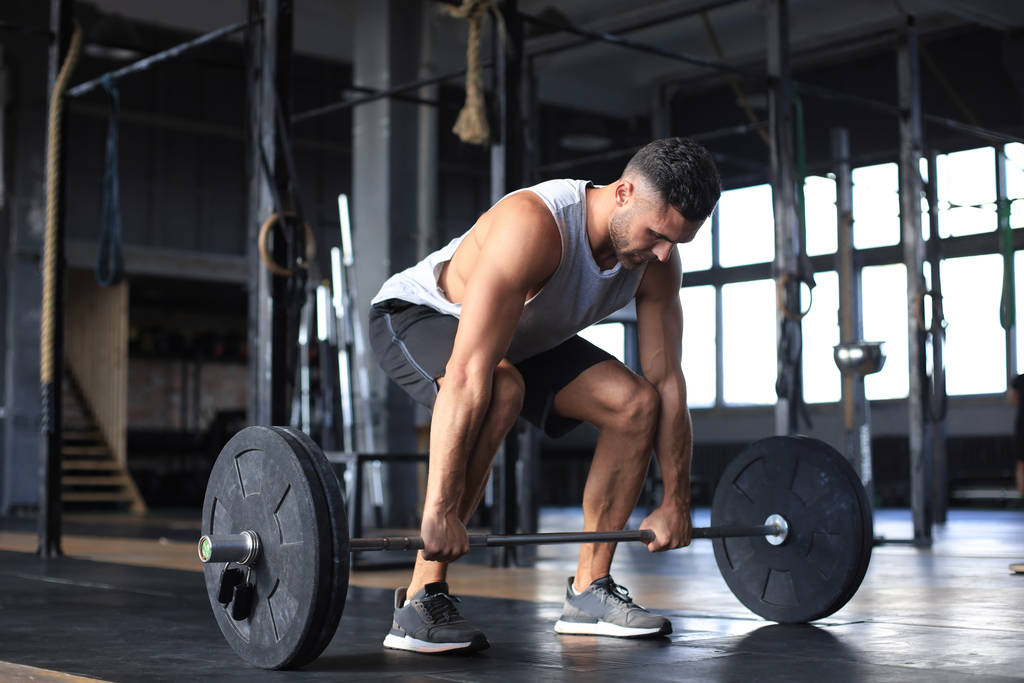 Мускулистый человек тренируется в спортзале, делая упражнения с штангой на бицепсах
. - Фото, изображение