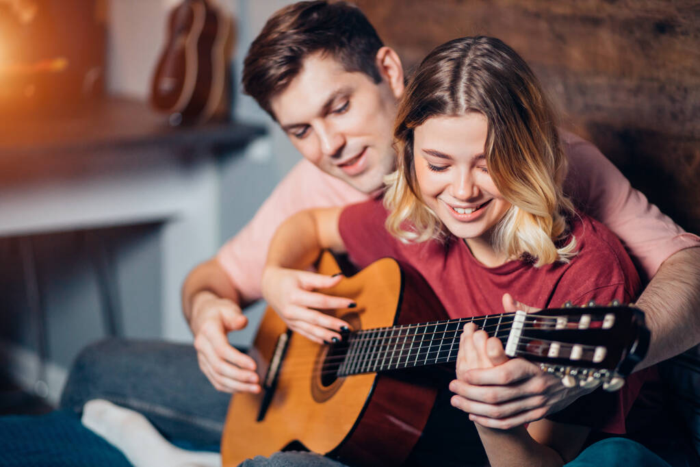 mooi meisje en knappe jongen spelen gitaar samen thuis - Foto, afbeelding