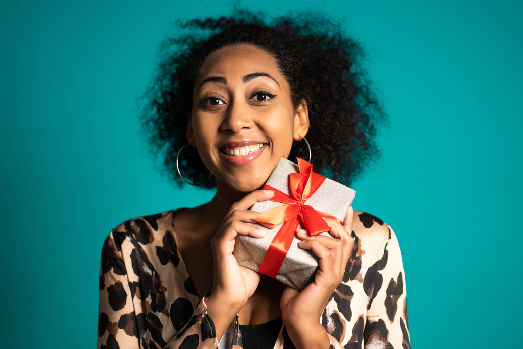 Mooie Afro-Amerikaanse vrouw kreeg een geschenkdoos met strik. Ze is blij en gevleid door aandacht. Meisje op studio achtergrond. - Foto, afbeelding