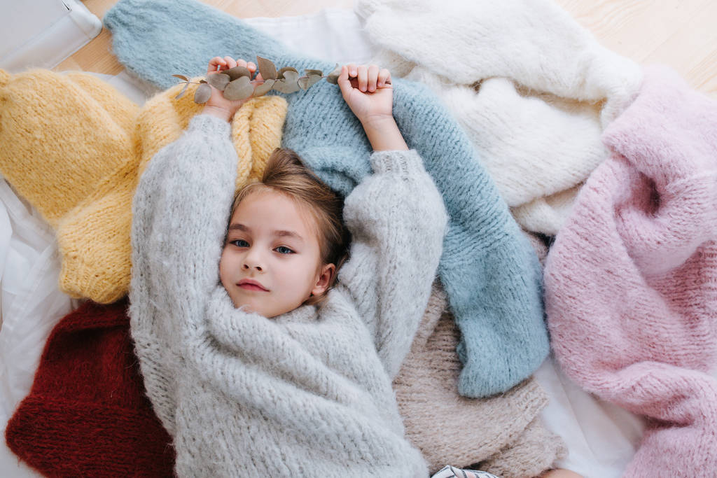 schläfriges kleines Mädchen liegt auf einem Stapel weicher mehrfarbiger Pullover - Foto, Bild