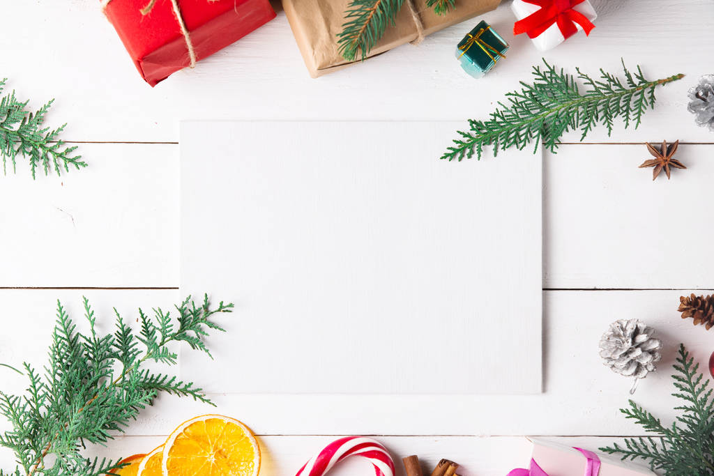 クリスマスギフトボックス、雪のモミの枝、針葉樹コーン、ドライフルーツ、休日の装飾、キャラメルスティックと木製の白い背景に美しいクリスマスの組成。新年。トップビュー、コピースペース. - 写真・画像