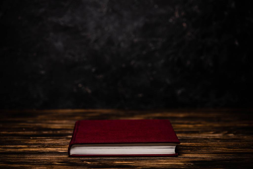 黒い背景の木のテーブルの上の赤い本 - 写真・画像