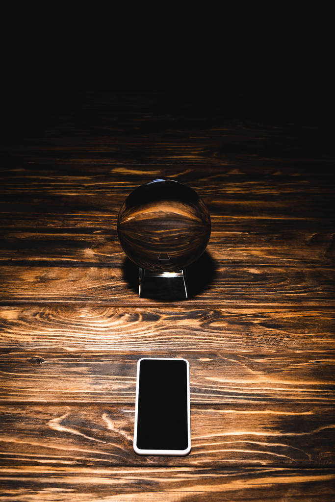 κρυστάλλινη σφαίρα με smartphone σε ξύλινο τραπέζι σε μαύρο φόντο - Φωτογραφία, εικόνα