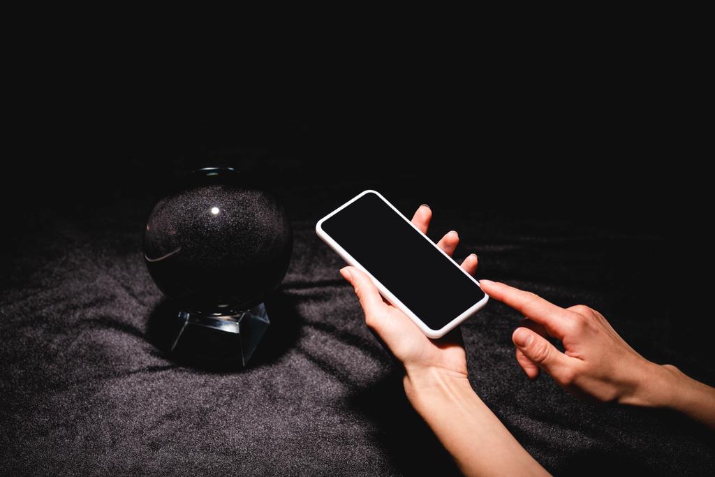 Siyah kadife kumaş üzerinde kristal kürenin yanında akıllı telefon tutan astrolog görüntüsü. - Fotoğraf, Görsel