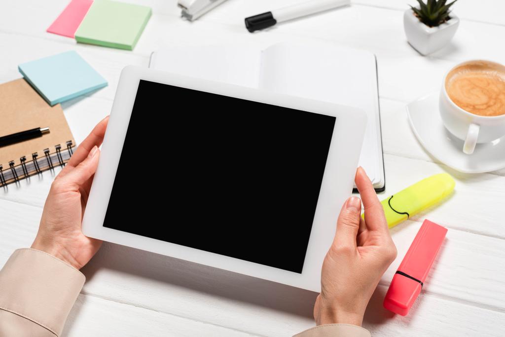 abgeschnittene Ansicht einer Frau, die am Arbeitsplatz ein digitales Tablet mit Bürobedarf und Kaffee in der Hand hält - Foto, Bild