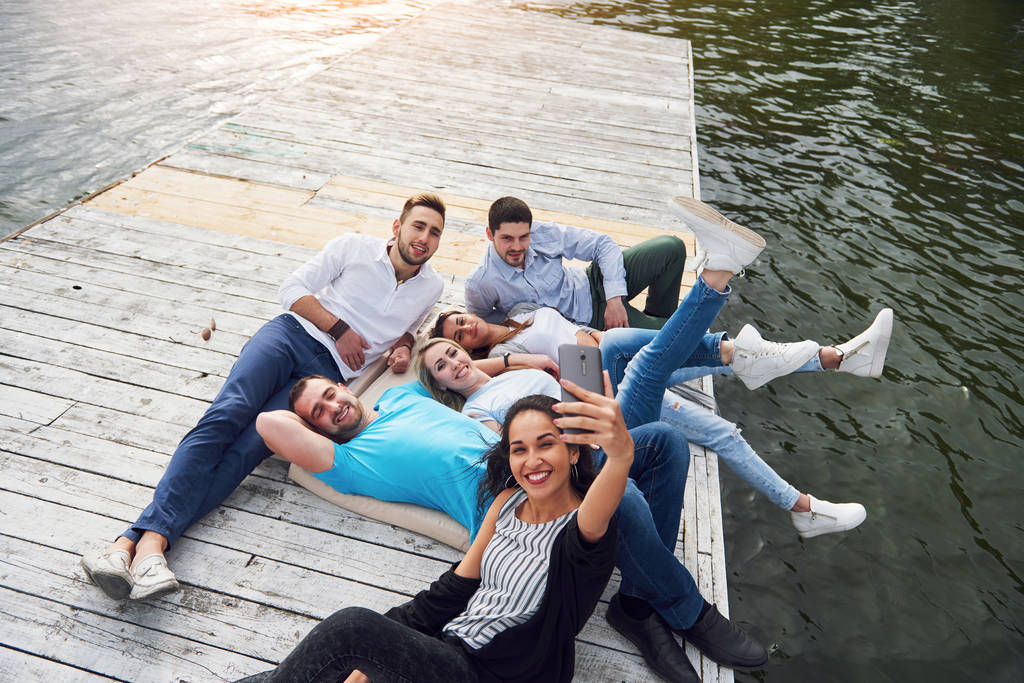 Grupa pięknych młodych ludzi, którzy robią Selfie leżące na molo, najlepsi przyjaciele dziewcząt i chłopców z koncepcją przyjemności tworzy emocjonalne życie ludzi - Zdjęcie, obraz