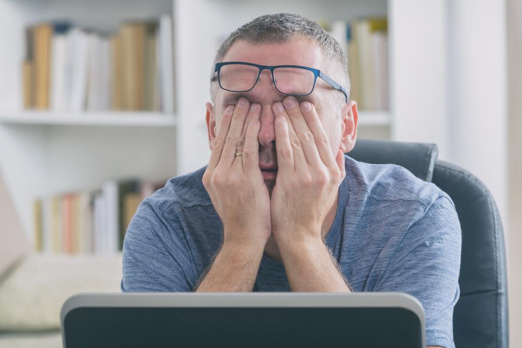 Tired freelancer man rubbing his eye due to digital eye strain