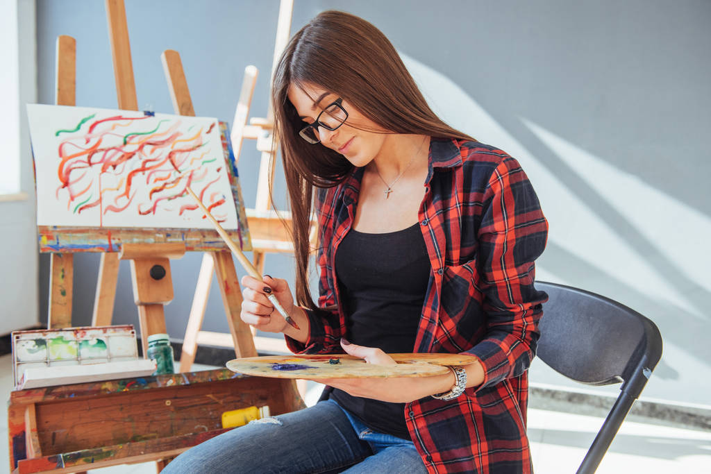 Όμορφη καλλιτέχνης κορίτσι ζωγραφίζει σε καμβά ζωγραφική στο καβαλέτο. - Φωτογραφία, εικόνα
