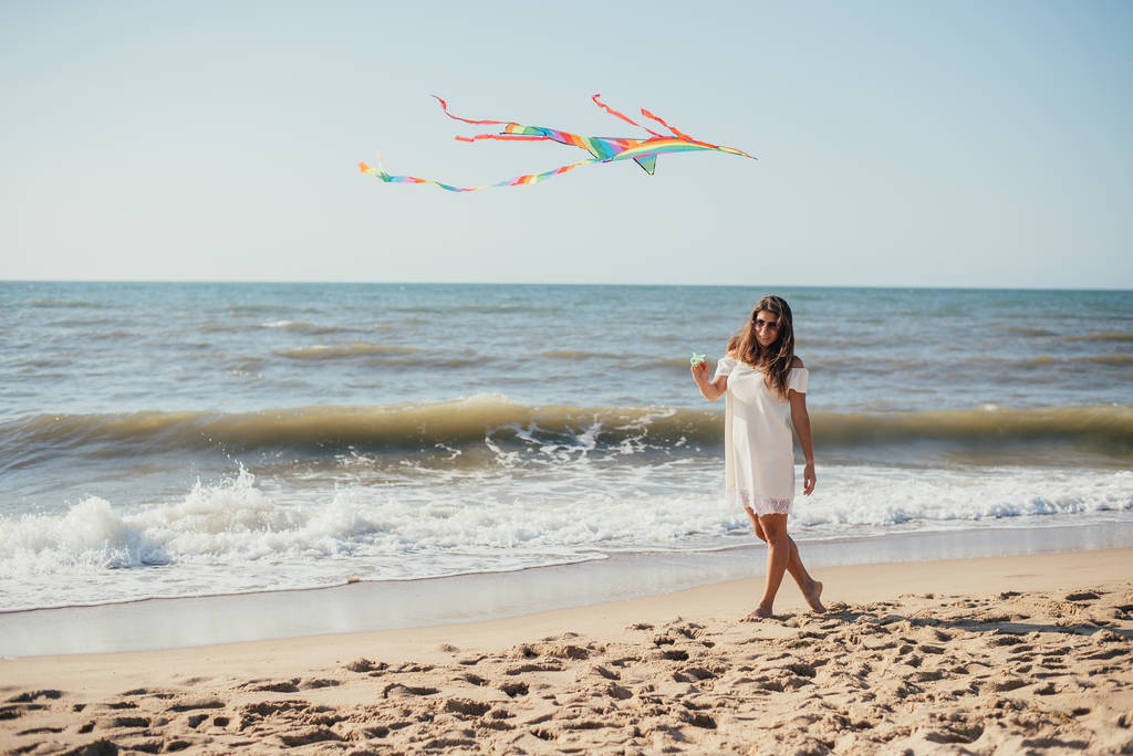 hermosa mujer joven feliz sosteniendo cometa colorida y caminando en la playa de arena
 - Foto, Imagen