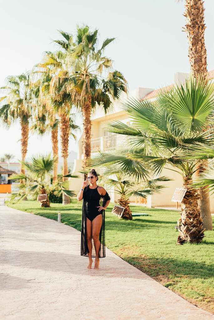 hermosa mujer joven caminando entre palmeras en el complejo tropical
 - Foto, Imagen