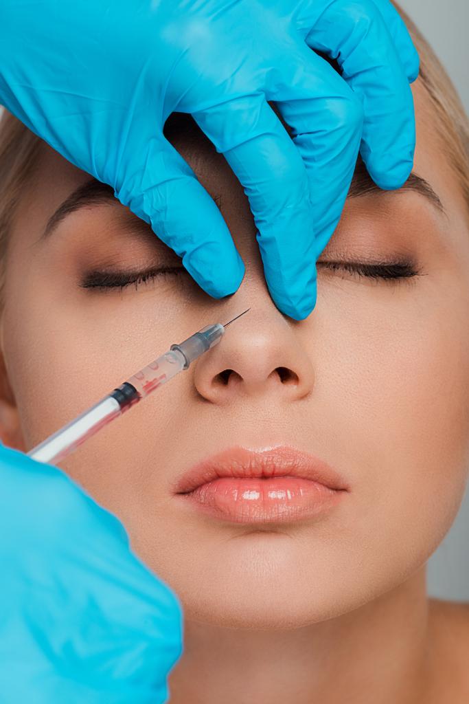 cropped view of beautician in latex gloves holding syringe near nose of girl with closed eyes - Photo, Image