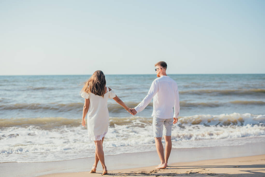 terug uitzicht op mooi gelukkig jong paar hand in hand op zandstrand in de zomer   - Foto, afbeelding